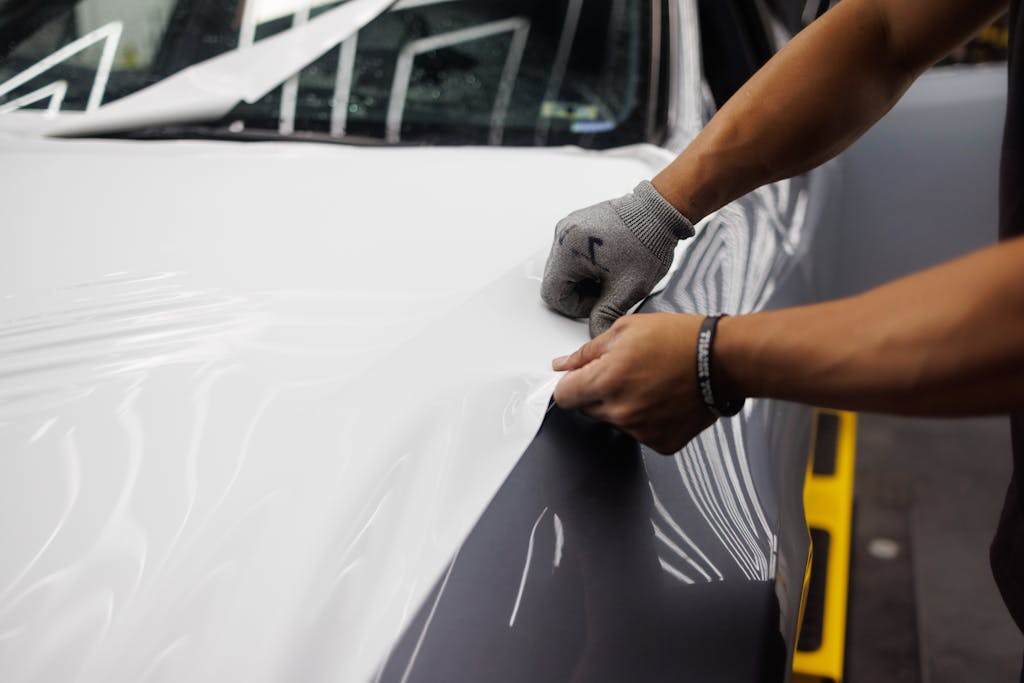 Close-up of hands applying vinyl wrap to a car hood, showcasing customization.